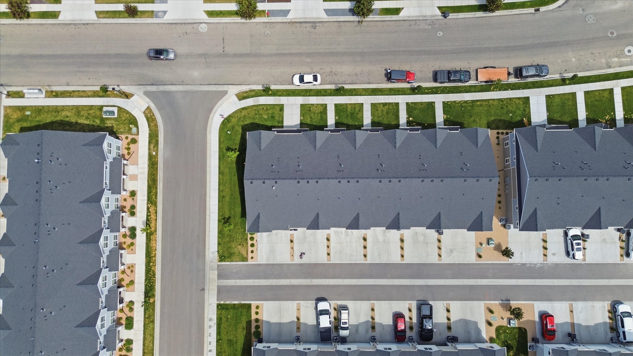 Residential development featuring multiple townhome-style buildings with dark gray shingle roofs, individual concrete driveways, and landscaped green spaces
