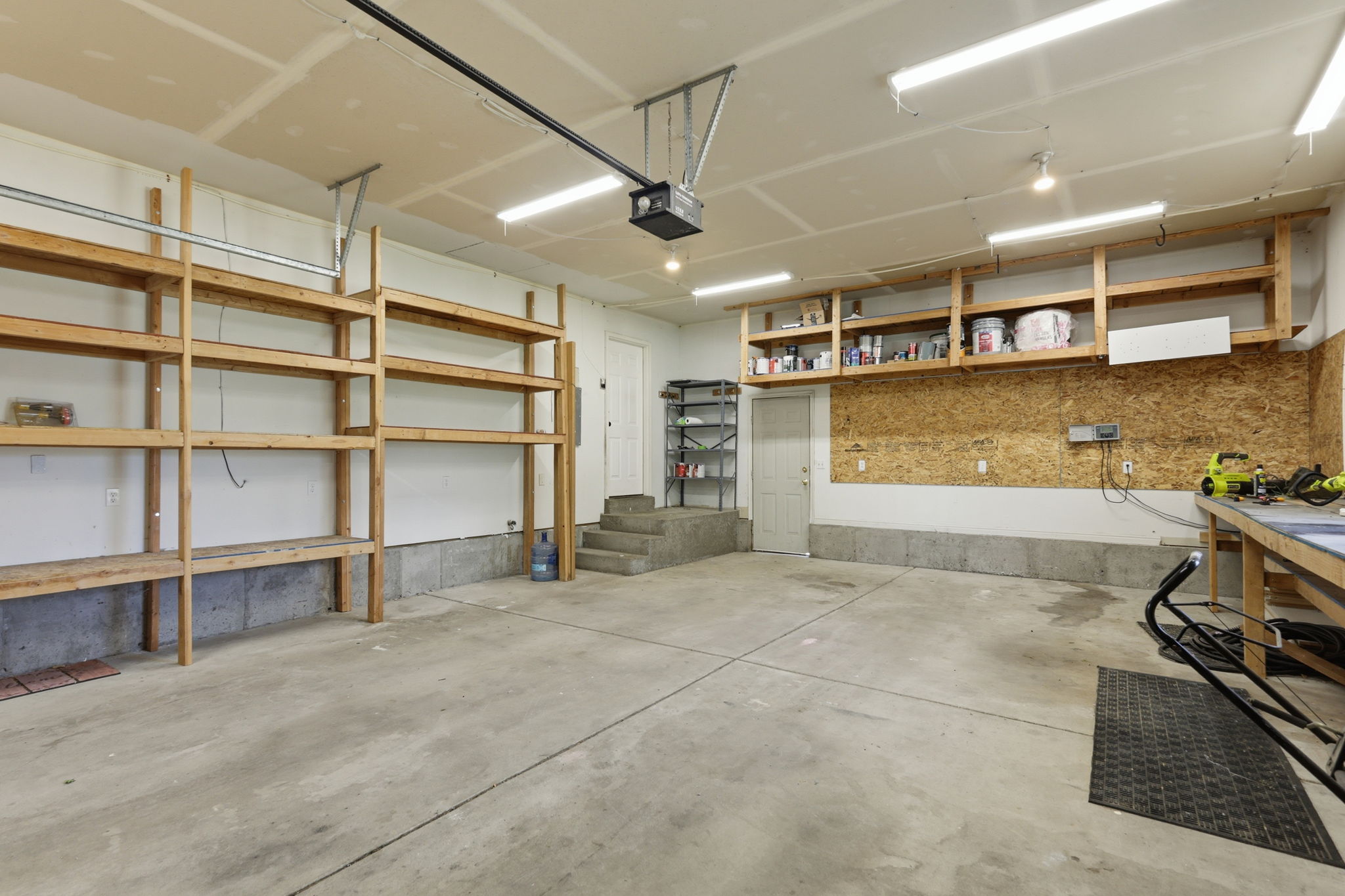 Spacious garage featuring a concrete floor, built-in wooden shelving, overhead lighting, and a utility door