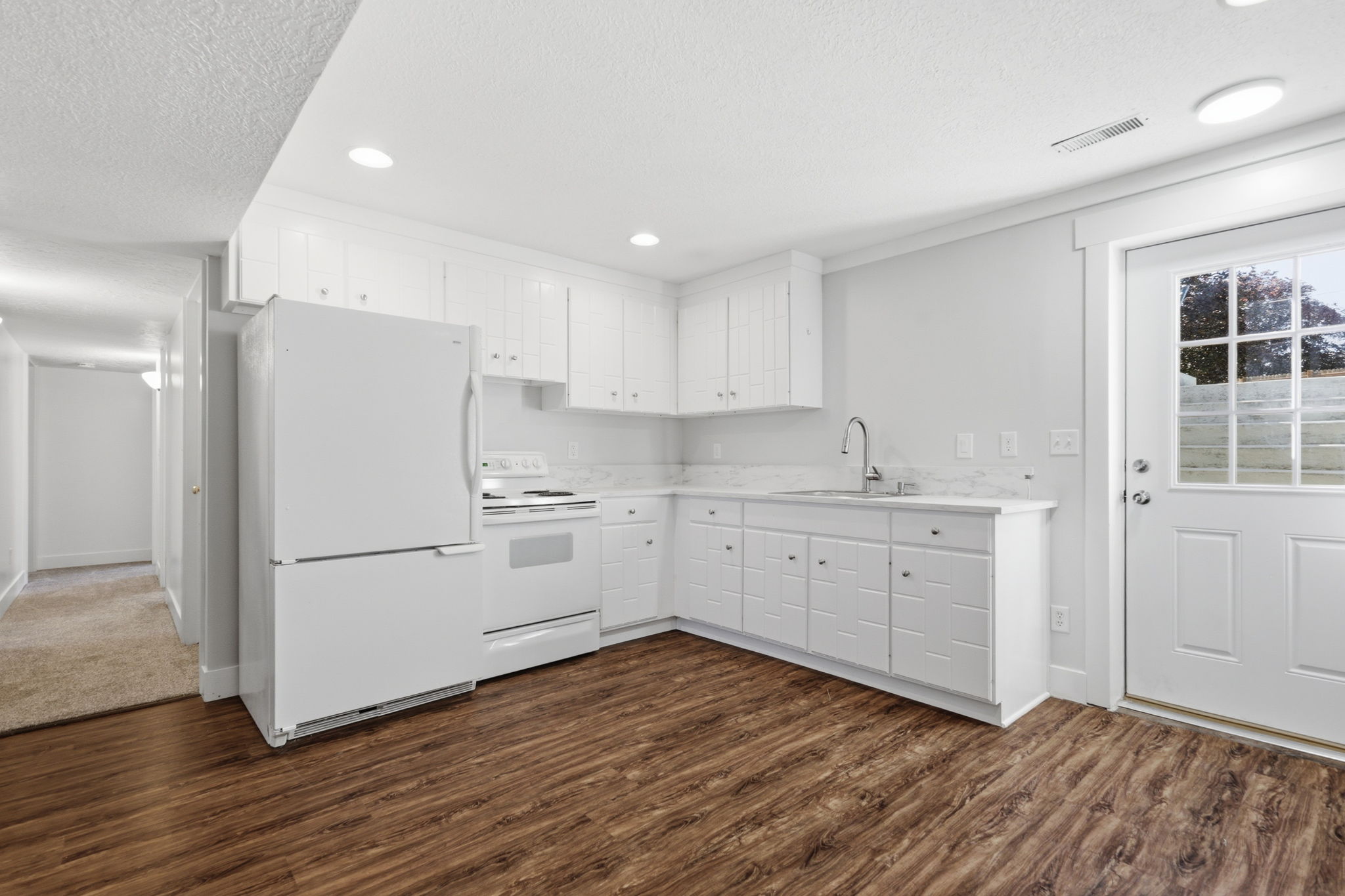 Kitchen area featuring wood-finish flooring, white cabinetry with silver-tone hardware, white appliances, and a glass-paneled exterior door