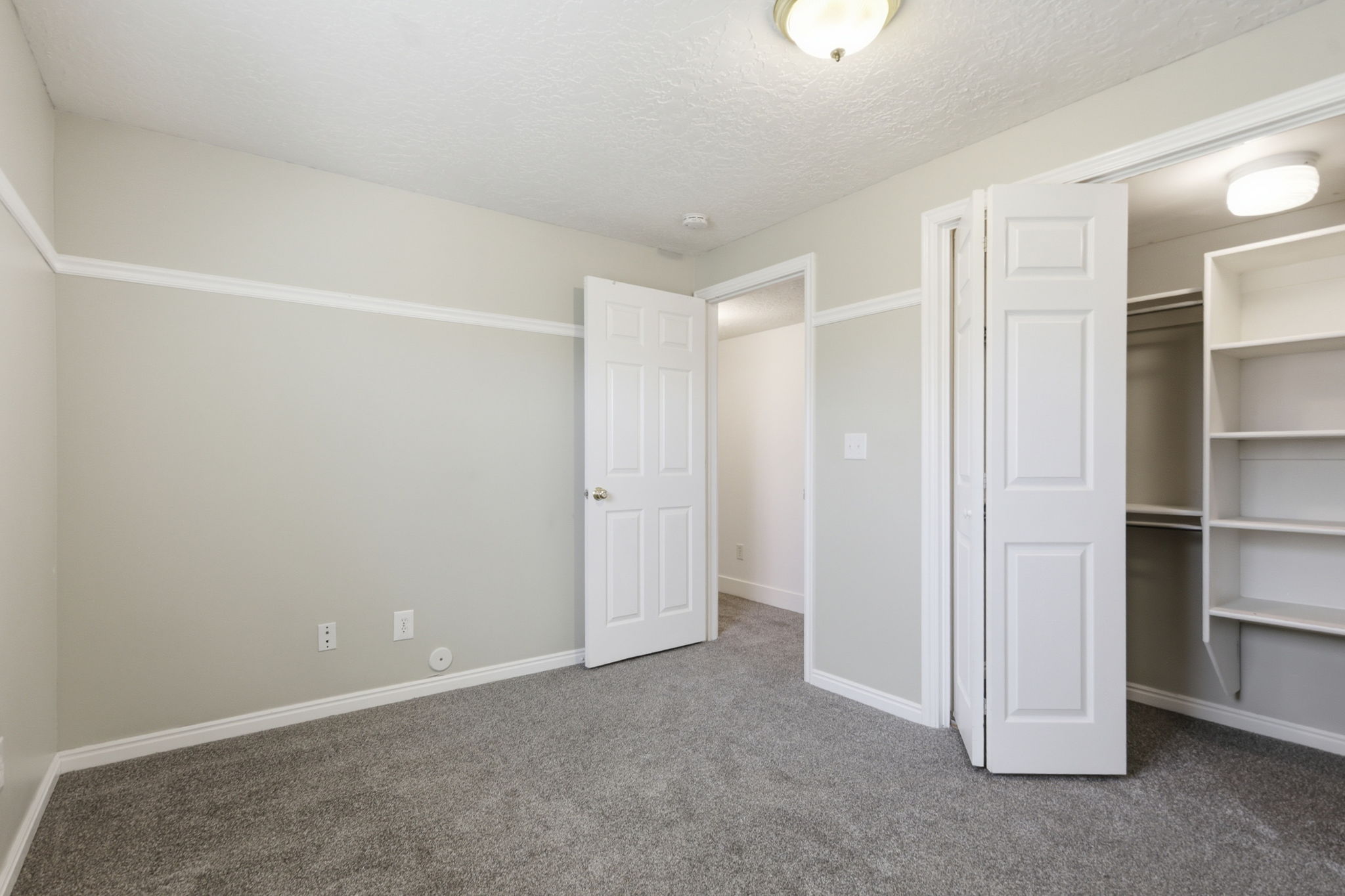 Room featuring light-toned walls with a chair rail, gray carpet flooring, and white baseboards