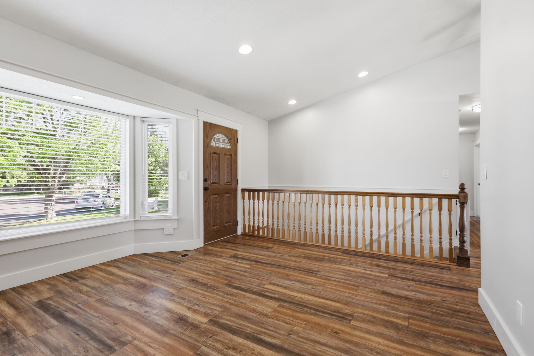 Entry space featuring wood-finish flooring, a bay window with blinds, and a traditional wood baluster railing