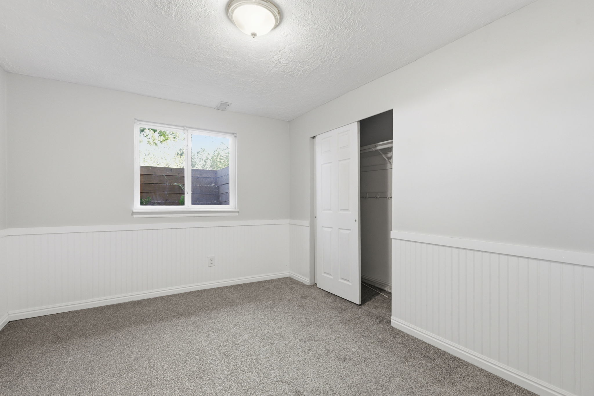 Carpeted room featuring beadboard wainscoting, a window with exterior visibility, a ceiling-mounted light fixture, and a sliding door closet with wire shelving