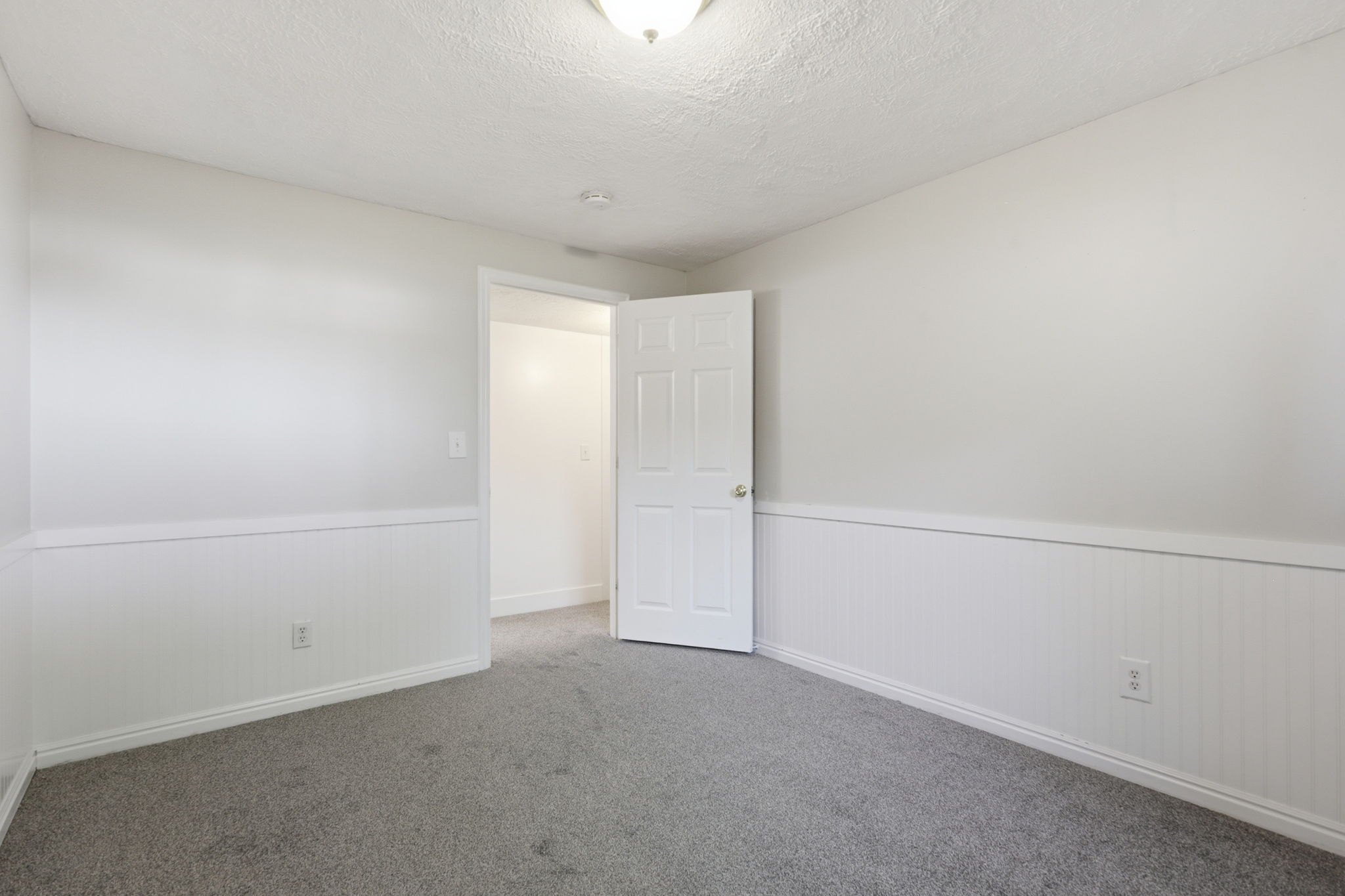 Room featuring gray carpet, white walls, and wainscoting