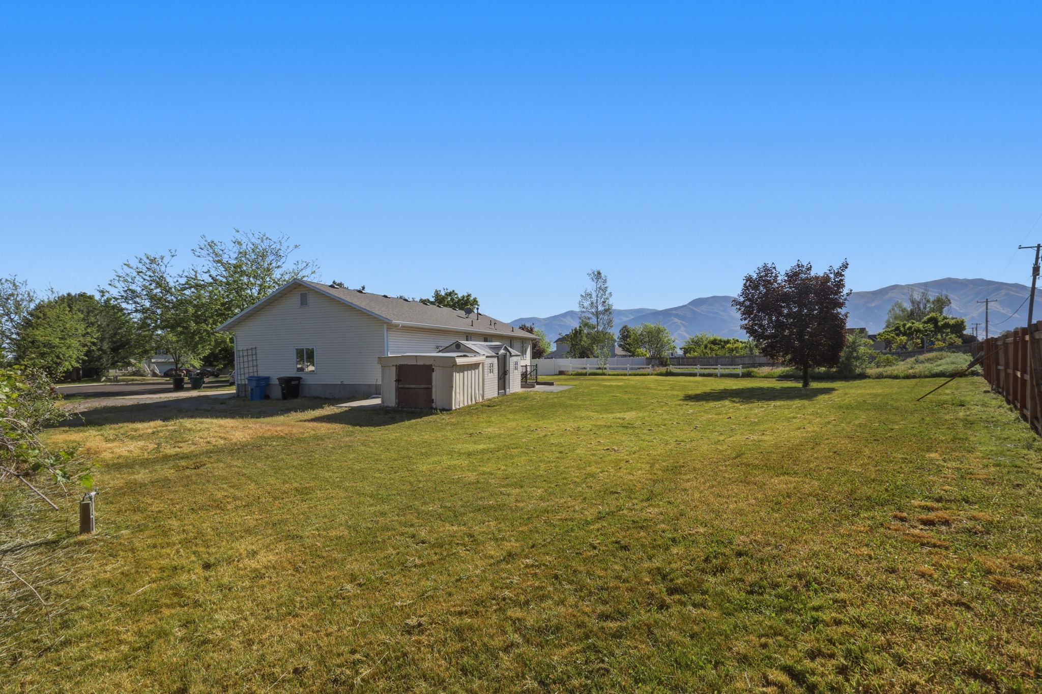 Expansive backyard with a large grassy area, mature trees, mountain backdrop, and wood fencing