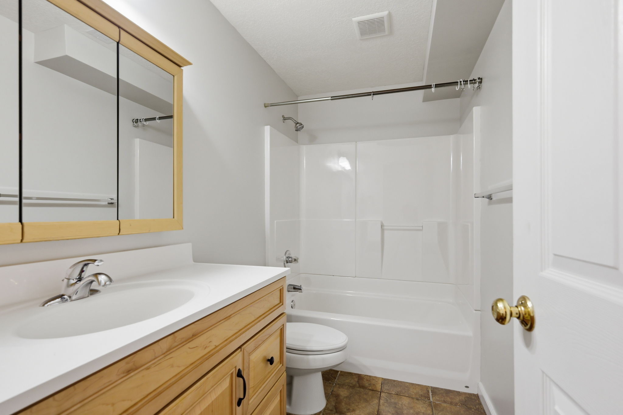 Bathroom featuring a light wood vanity, white countertop with integrated sink, chrome faucet, and a large mirrored medicine cabinet