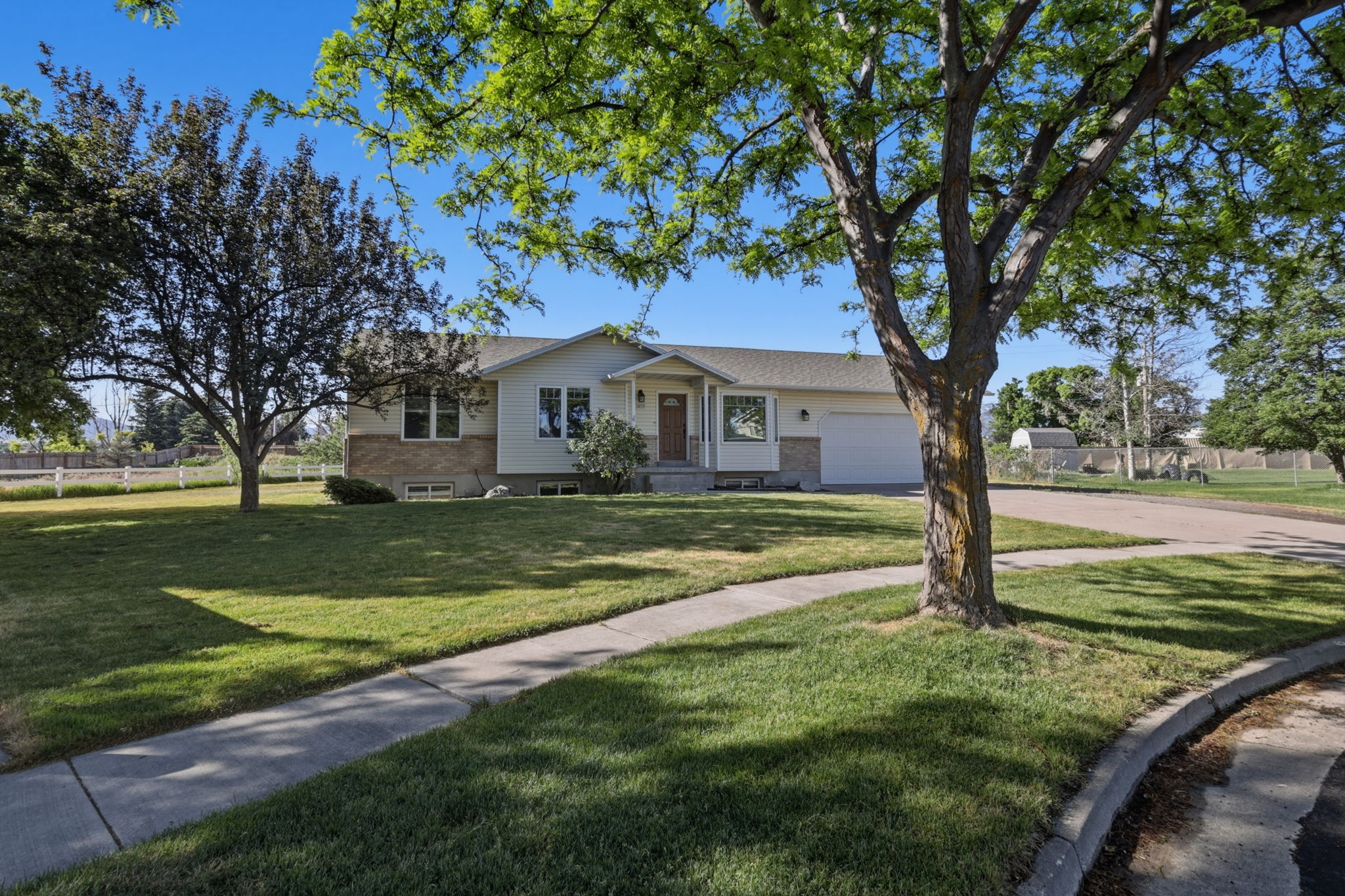Ranch-style residence featuring a prominent front lawn with mature trees, a two-tone exterior with a stone accent facade, an attached garage, and a concrete driveway