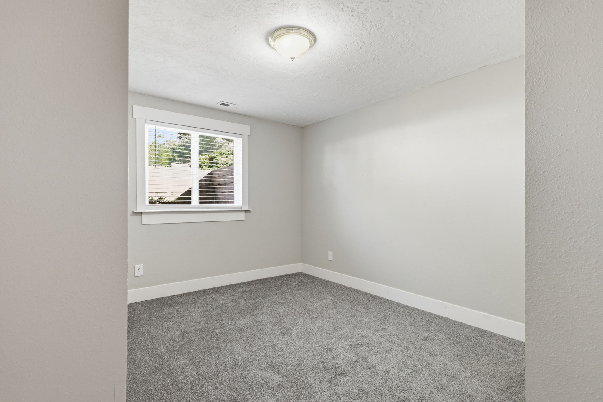 Light gray wall paint, gray carpet flooring, white trim, and a window with horizontal blinds