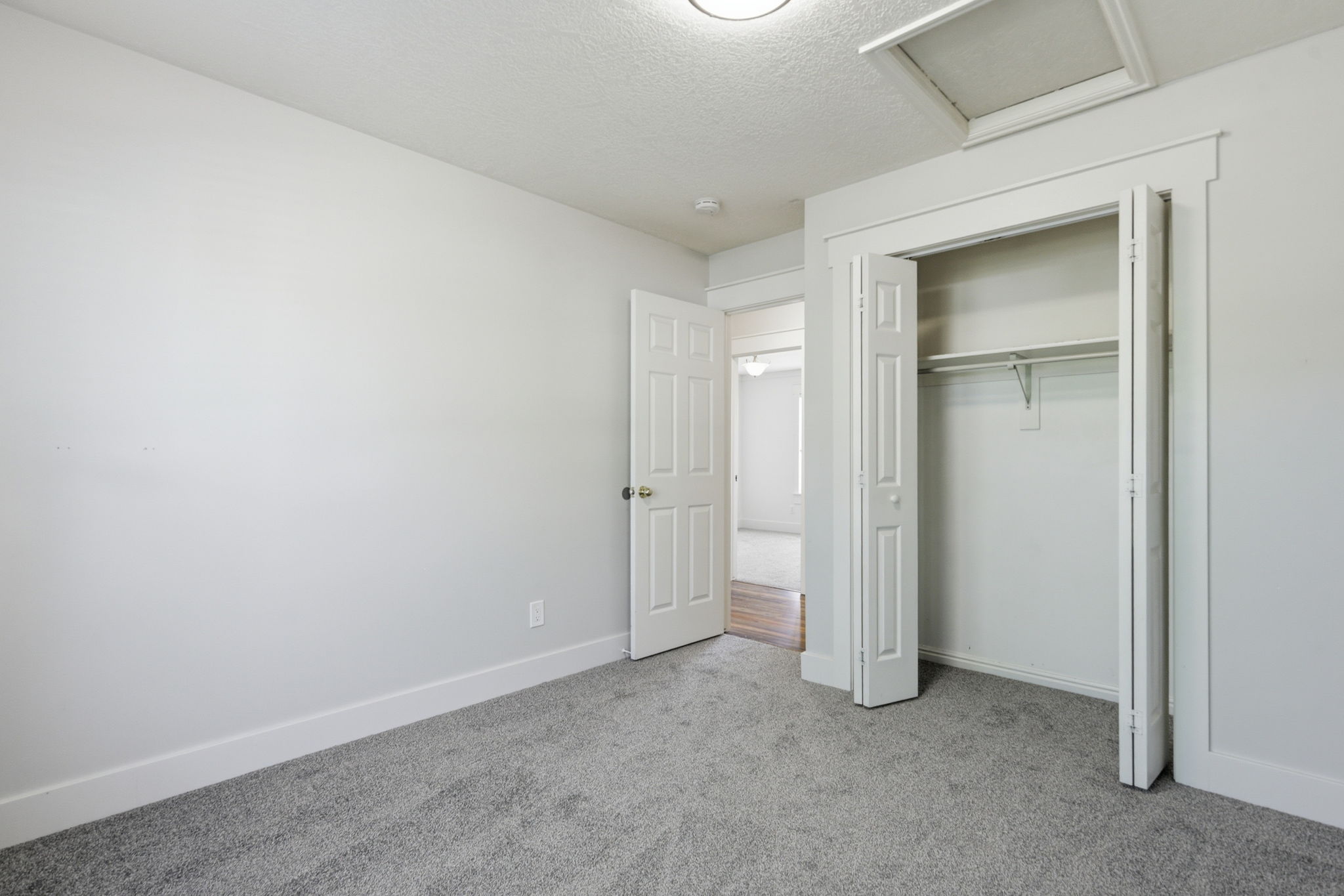 Neutral-toned room featuring grey textured carpeting, white baseboards, and a bi-fold closet with a hanging rod and shelving