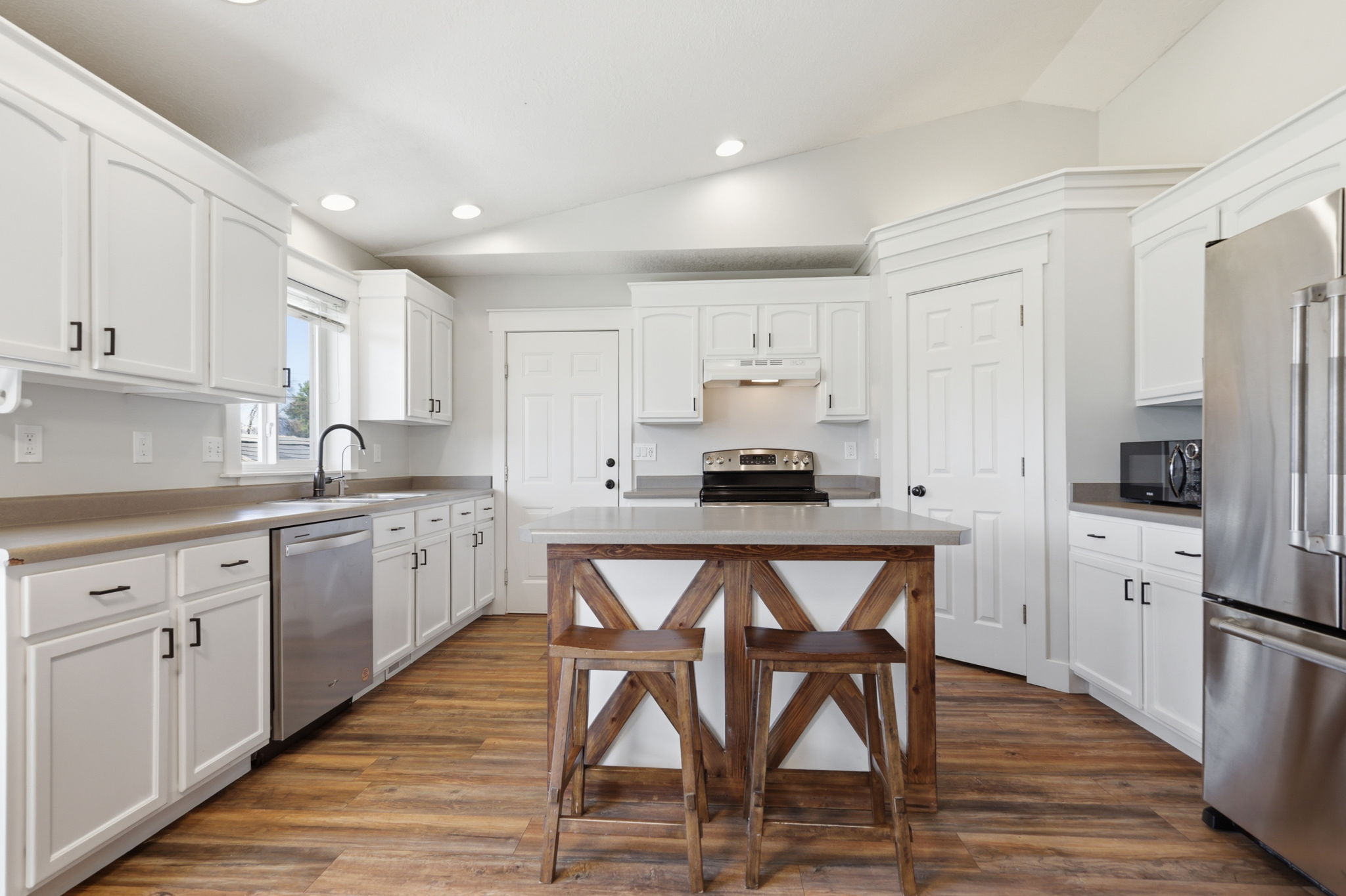 Kitchen featuring a rustic wood-finish island with a light-toned countertop, white cabinetry, stainless steel appliances, wood-finish flooring, and vaulted ceilings