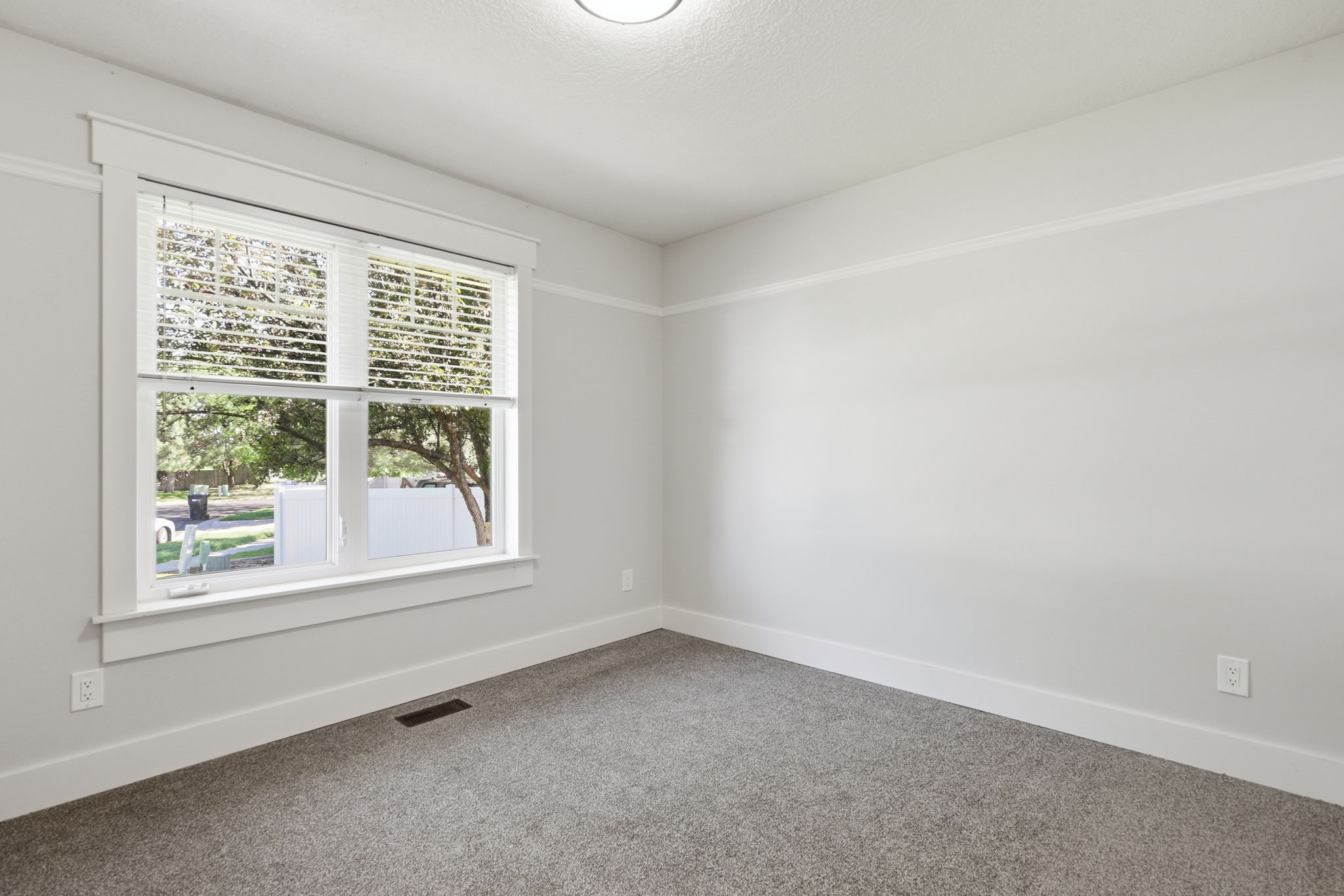 Room featuring a double window with white blinds, neutral gray wall color, textured gray carpet, and white trim work