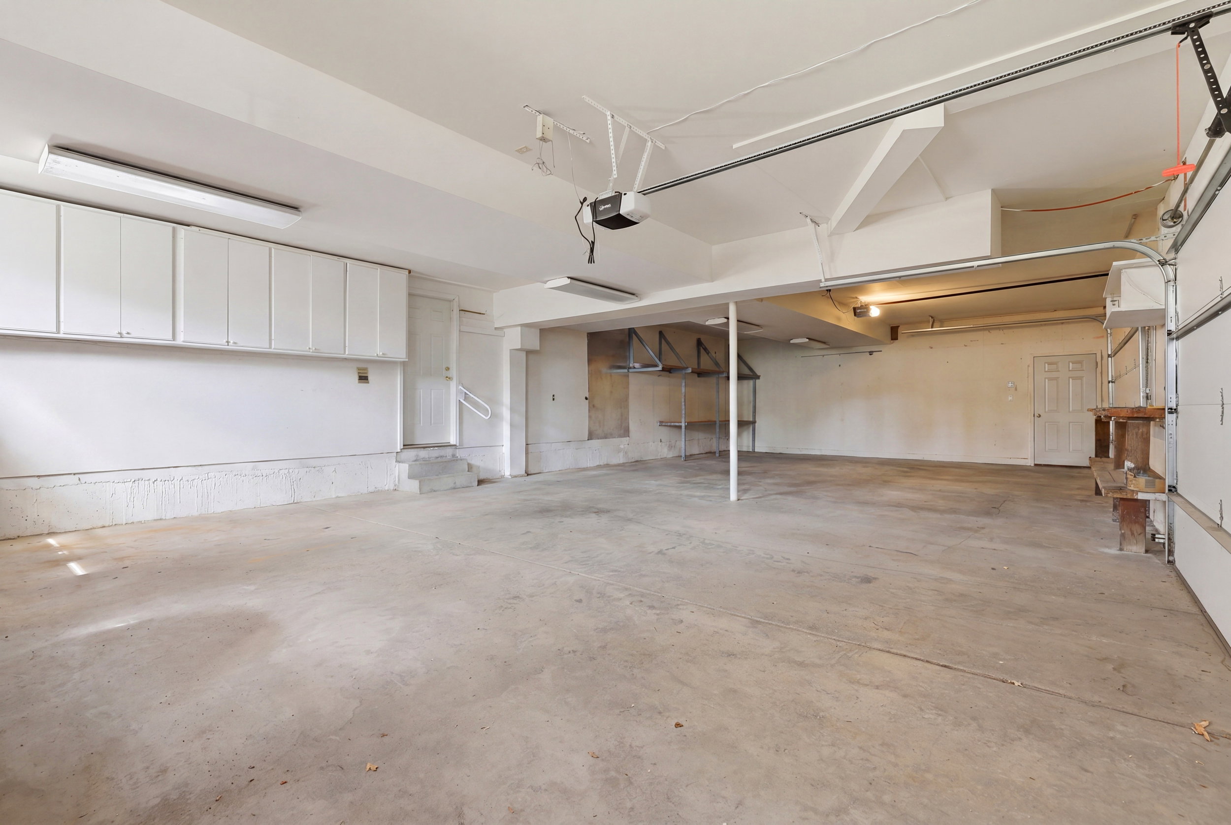 Spacious garage featuring a concrete floor, overhead fluorescent lighting, and extensive built-in white cabinetry