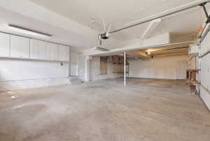 Spacious garage featuring a concrete floor, overhead fluorescent lighting, and extensive built-in white cabinetry