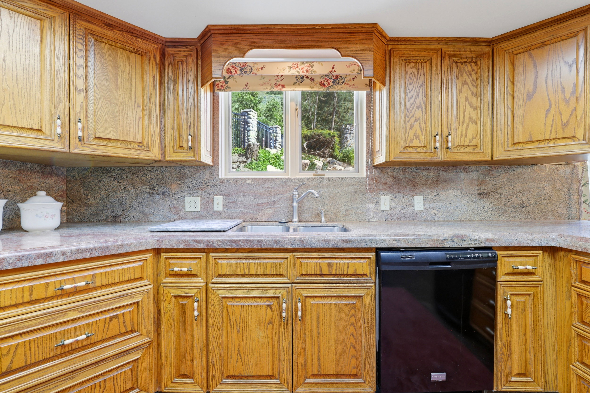 Kitchen featuring extensive wood cabinetry, coordinating stone countertops, a stainless steel double basin sink, and a black built-in dishwasher