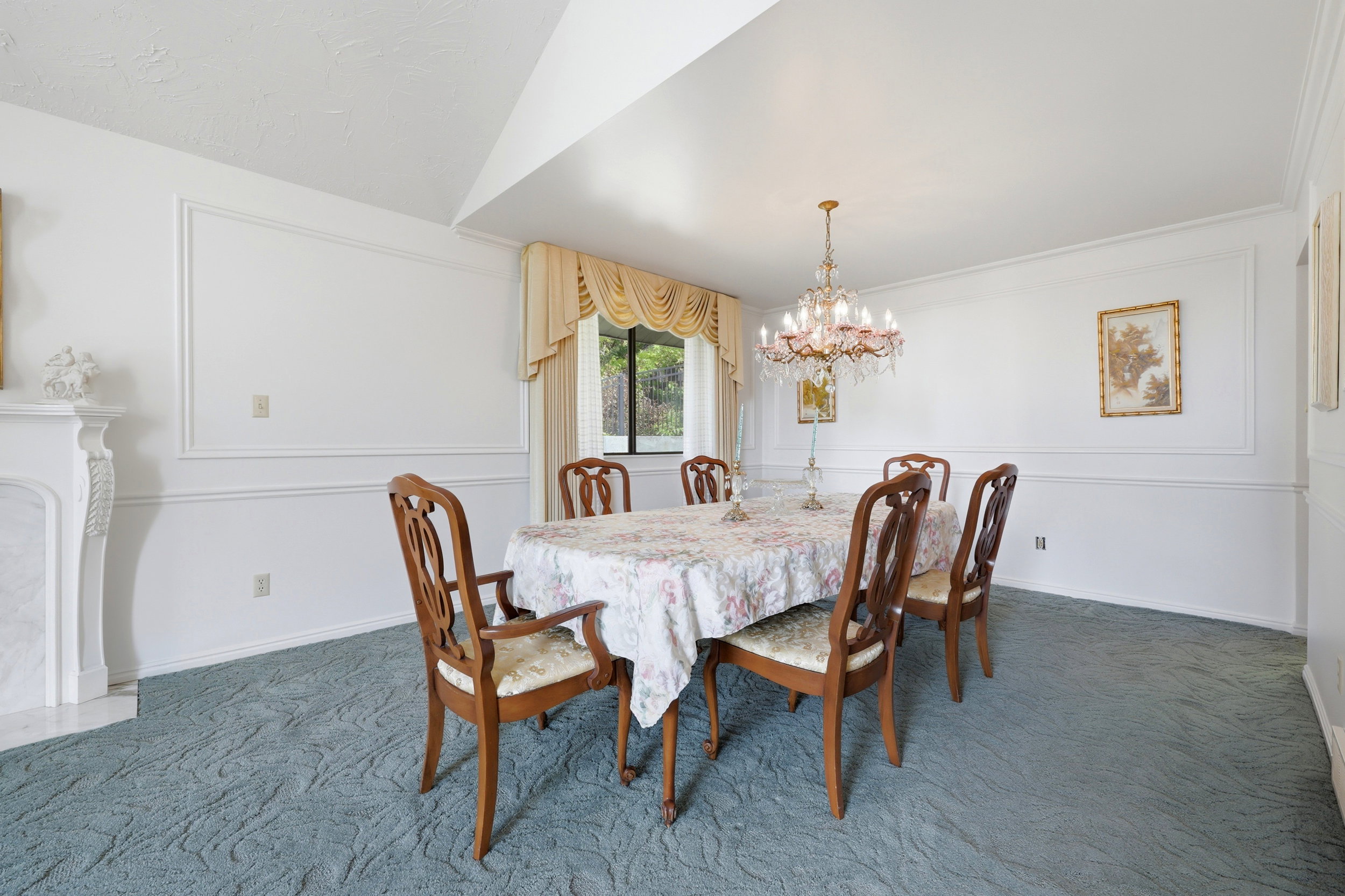 Formal dining area featuring a decorative chandelier, wainscoting, a mantel, a large window, and patterned carpeting