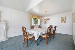 Formal dining area featuring a decorative chandelier, wainscoting, a mantel, a large window, and patterned carpeting