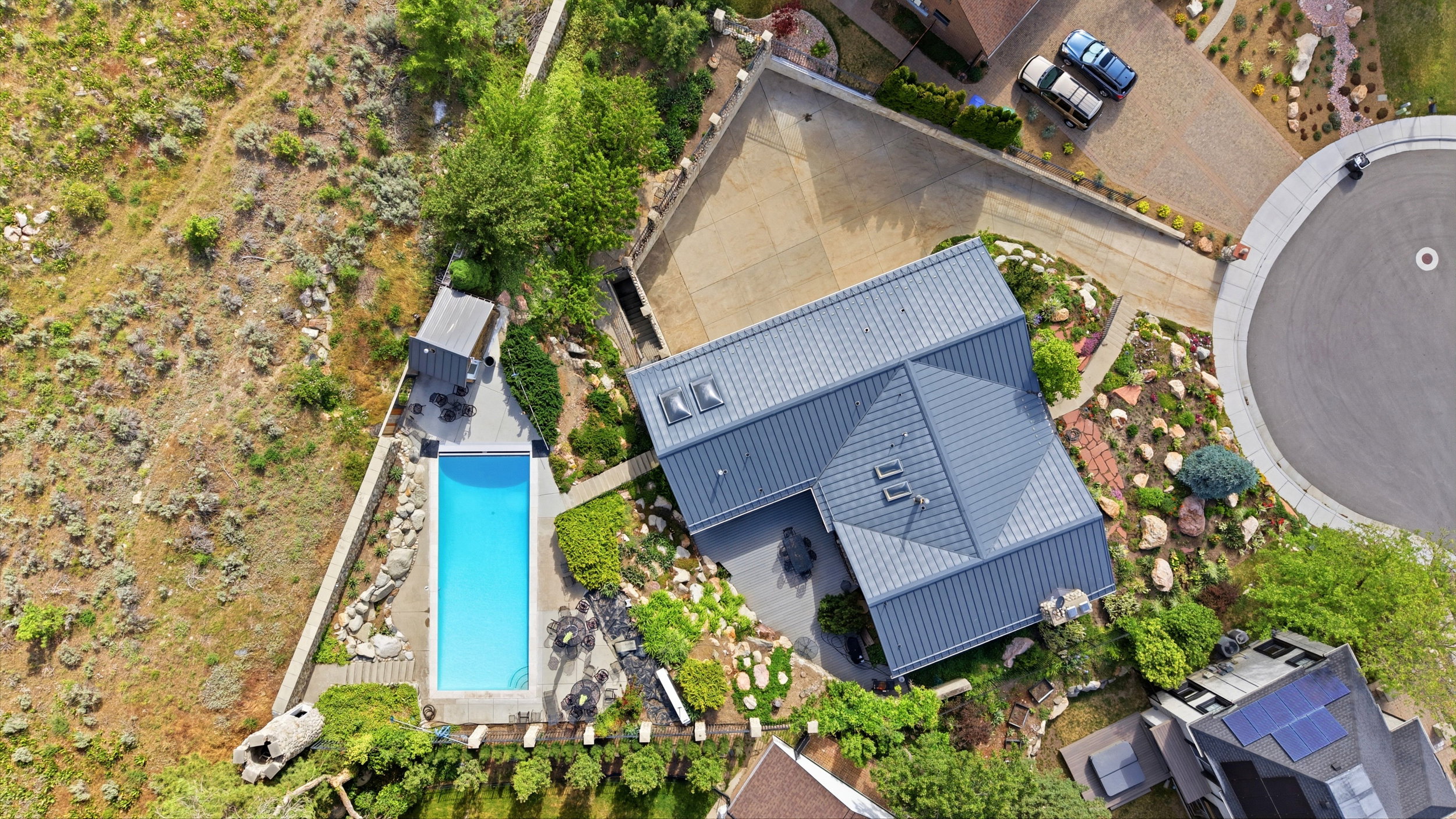 Modern metal roof residence featuring a rectangular swimming pool, terraced landscaping, and an attached paver driveway