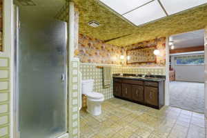 Bathroom featuring a glass-enclosed shower, a vanity with a dark wood-finish cabinet and dark countertop, a toilet, a rectangular mirror, and an overhead skylight