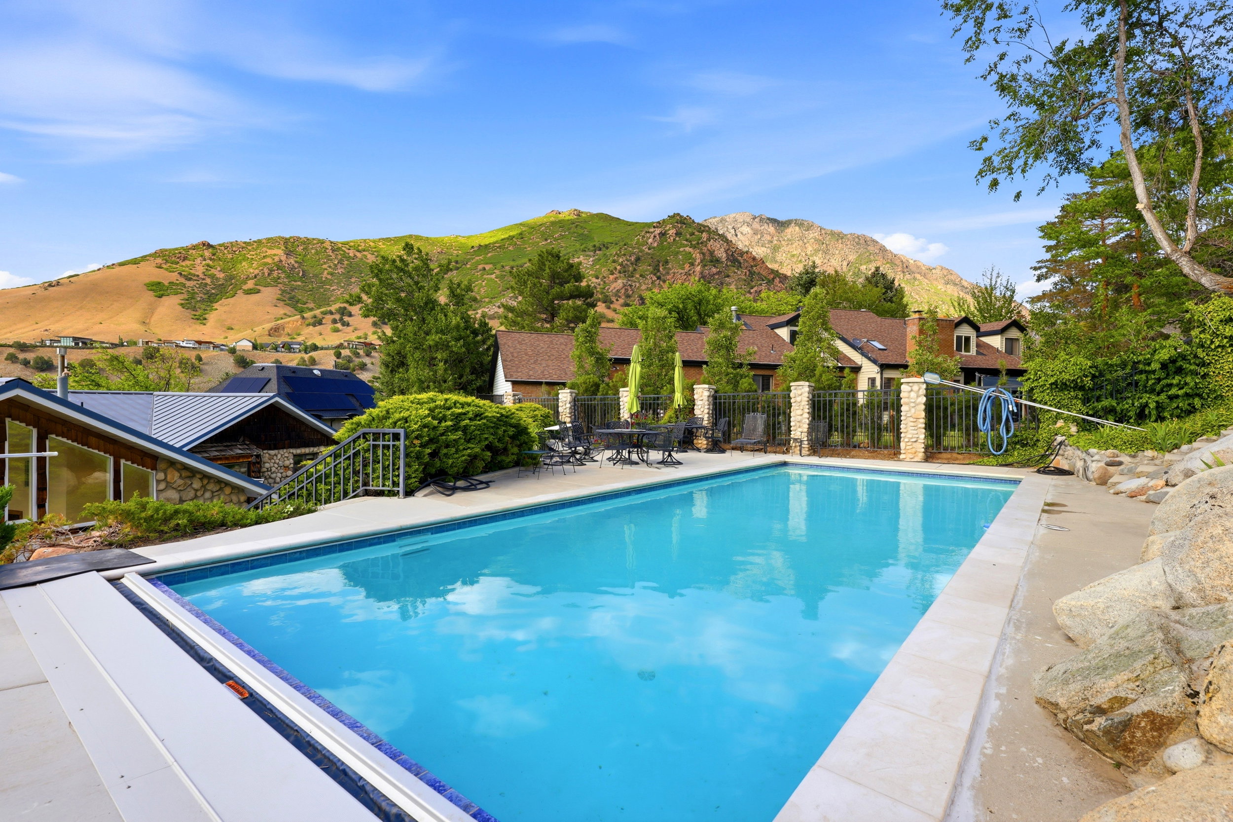 Outdoor swimming pool with integrated cover system, surrounded by a concrete patio and a metal fence with stone pillars