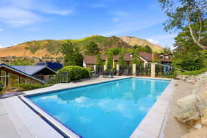 Outdoor swimming pool with integrated cover system, surrounded by a concrete patio and a metal fence with stone pillars