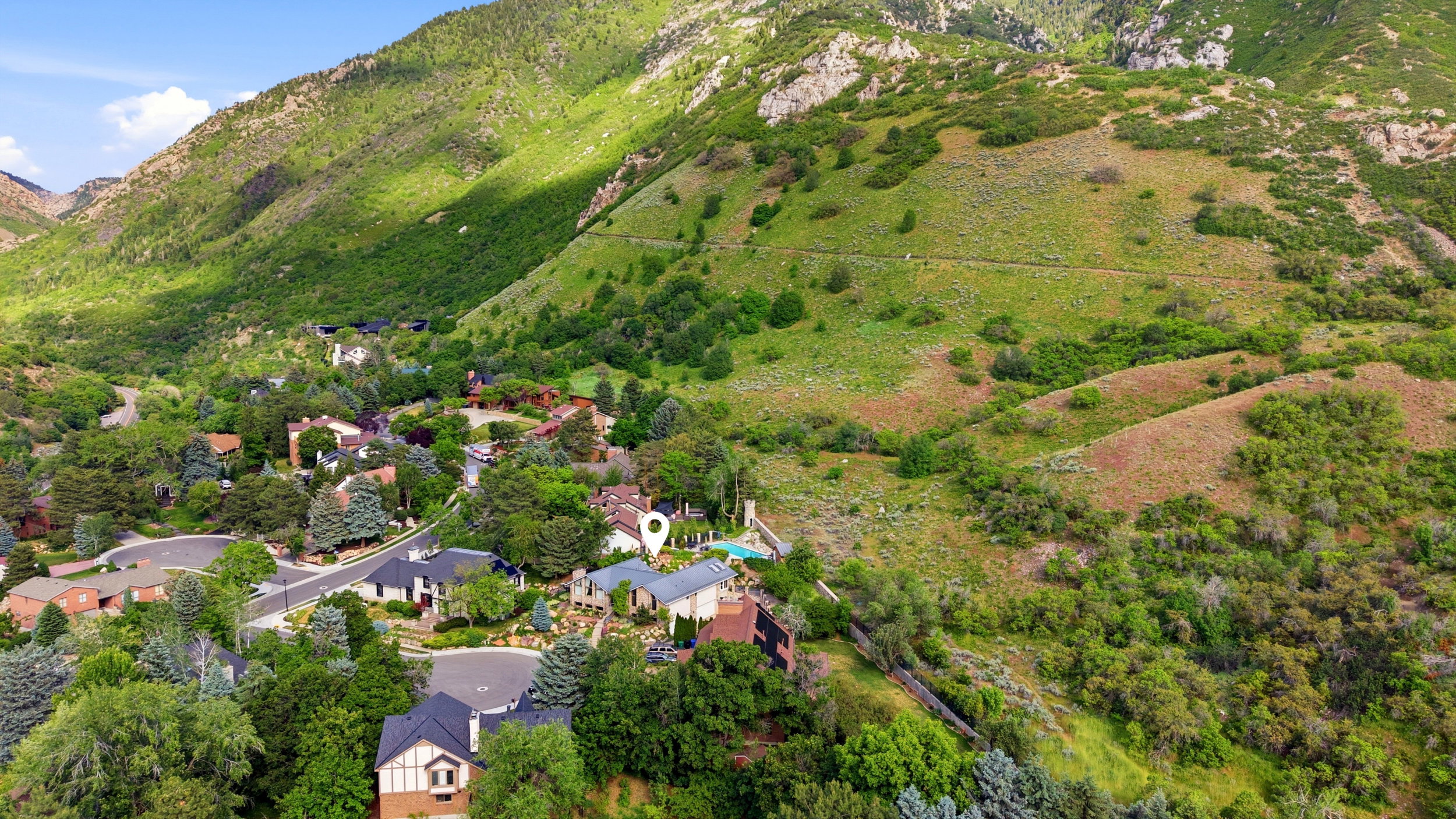 Landscaped property situated within a mountainous area, featuring mature trees and a residential street