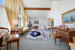 Spacious living area featuring exposed wood beams, a white mantel fireplace, and a large window with a stone surround