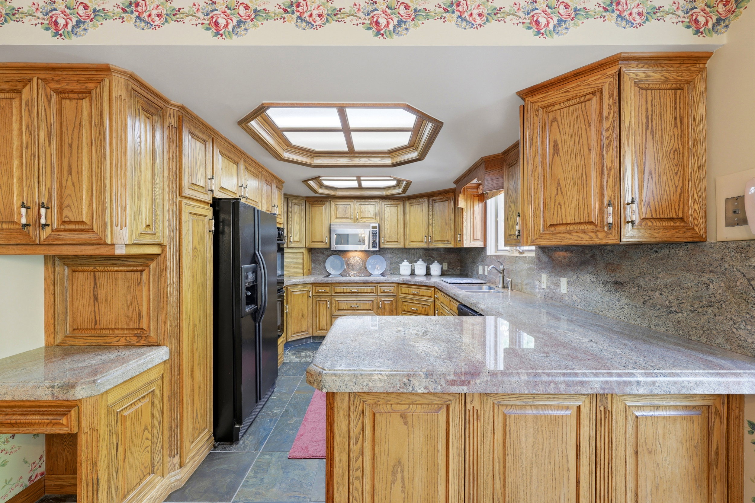 Spacious kitchen featuring extensive wood cabinetry, stone countertops, a built-in black refrigerator, and a stainless steel microwave