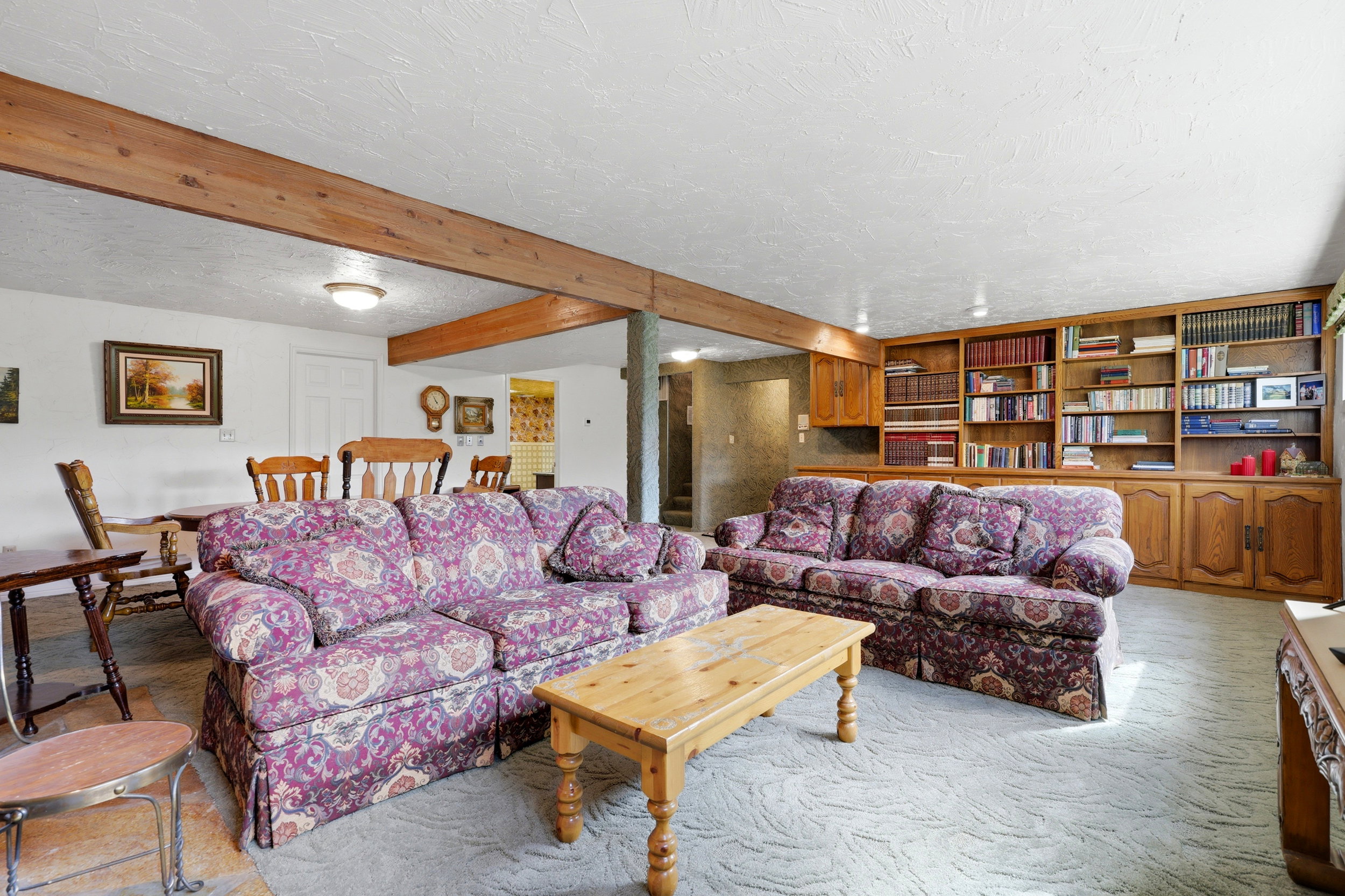 Wood-finish ceiling beams, built-in shelving, recessed and surface-mounted lighting, and neutral wall paint
