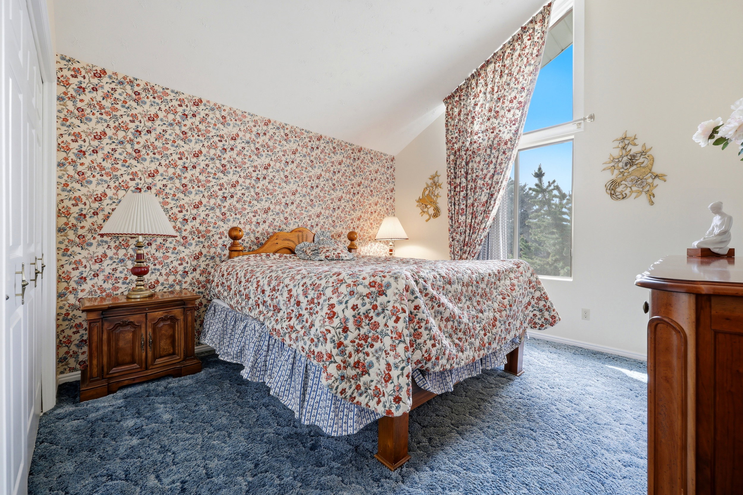 Angled ceiling bedroom with a prominent window, plush blue carpeting, and floral pattern wallpaper