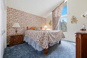 Angled ceiling bedroom with a prominent window, plush blue carpeting, and floral pattern wallpaper