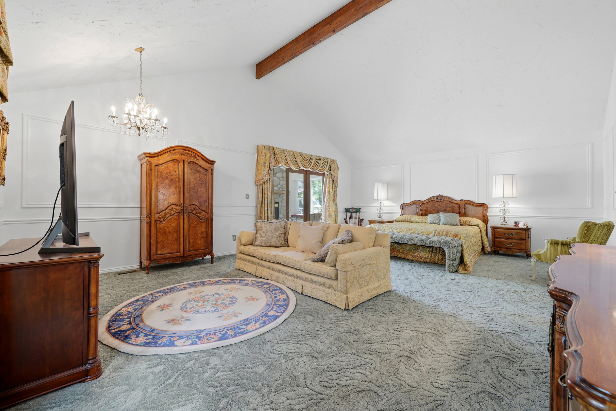Spacious room featuring vaulted ceilings with exposed wood beams, wall molding, and a decorative chandelier