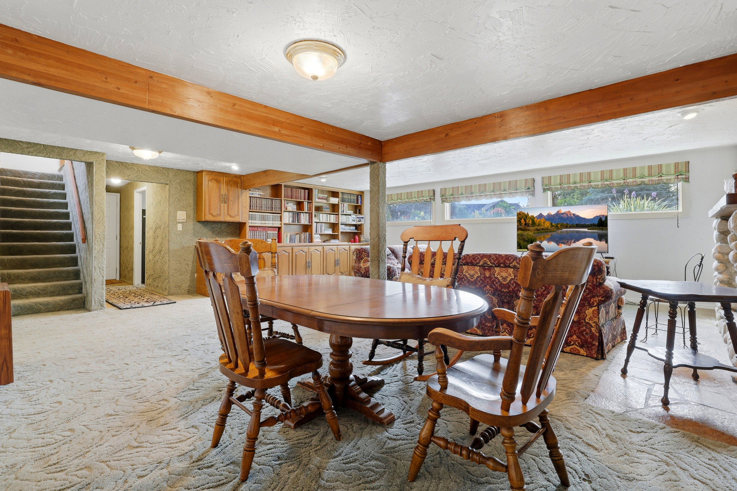 Finished lower level featuring exposed wood beams, built-in shelving, a stone-clad fireplace, and multiple windows