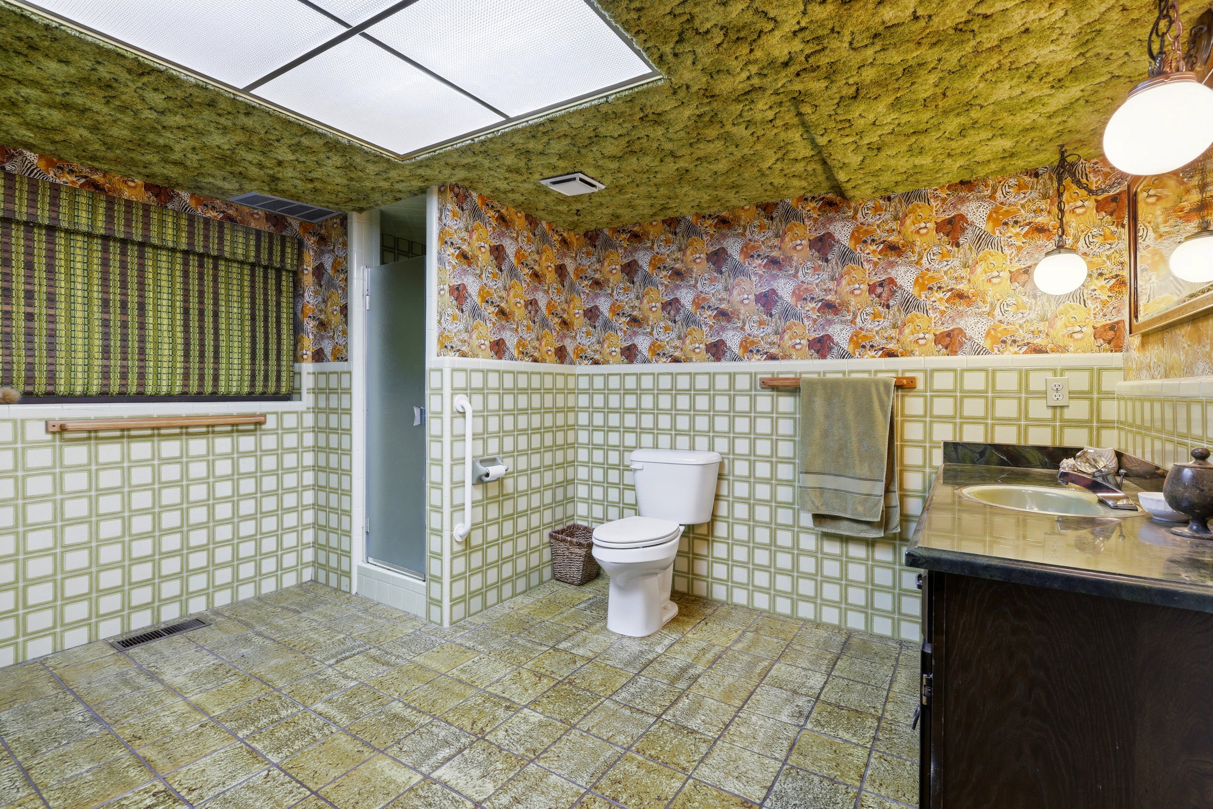 Bathroom featuring green square wall tiles, patterned wallpaper, and a wood-finish vanity with an integrated sink