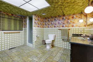 Bathroom featuring green square wall tiles, patterned wallpaper, and a wood-finish vanity with an integrated sink