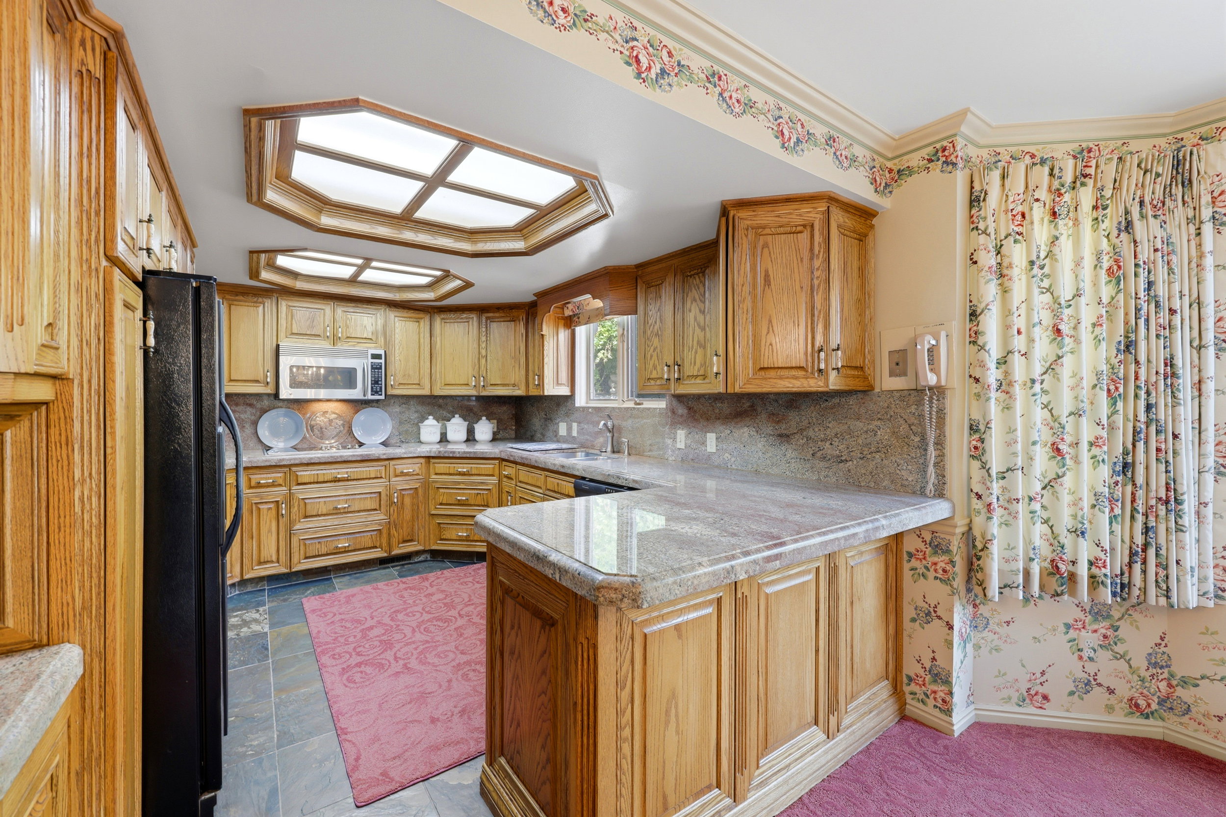 Kitchen featuring wood cabinetry, light-toned stone countertops, and a stone-finish tile backsplash