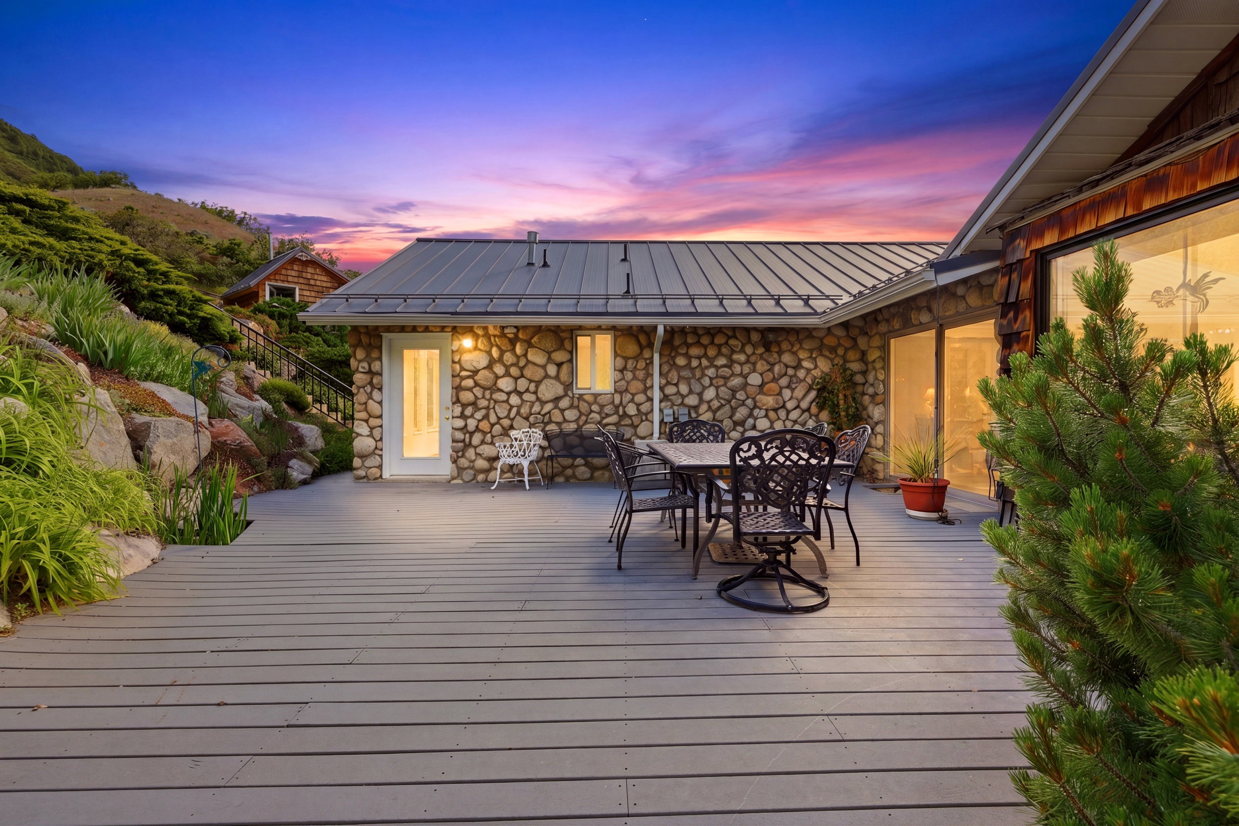 Expansive deck area featuring a gray wood-finish surface, stone wall construction, a metal roof, and large windows