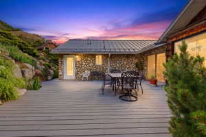 Expansive deck area featuring a gray wood-finish surface, stone wall construction, a metal roof, and large windows