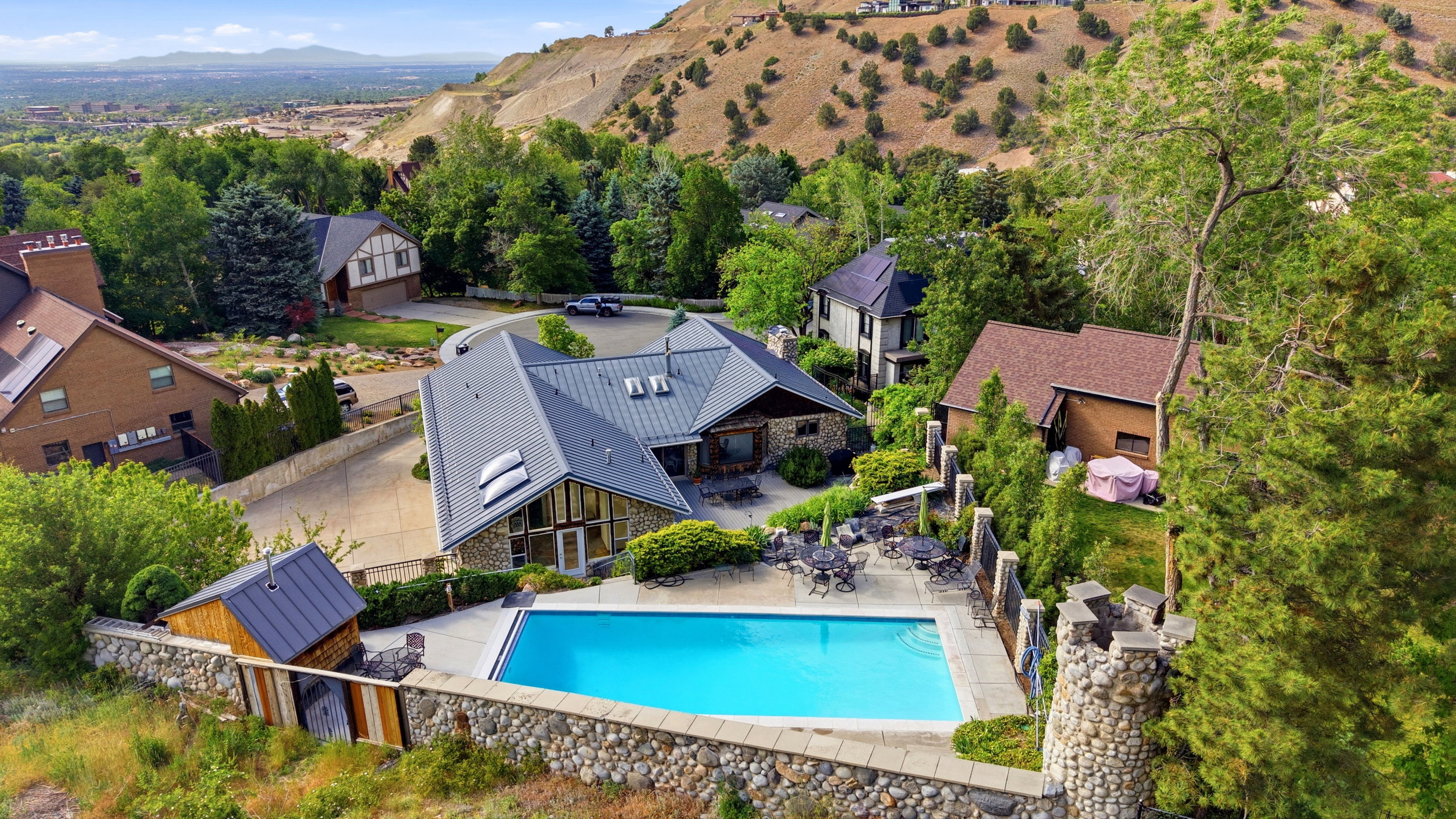 Expansive outdoor living area featuring a rectangular swimming pool, stone retaining walls, and a dedicated pool house