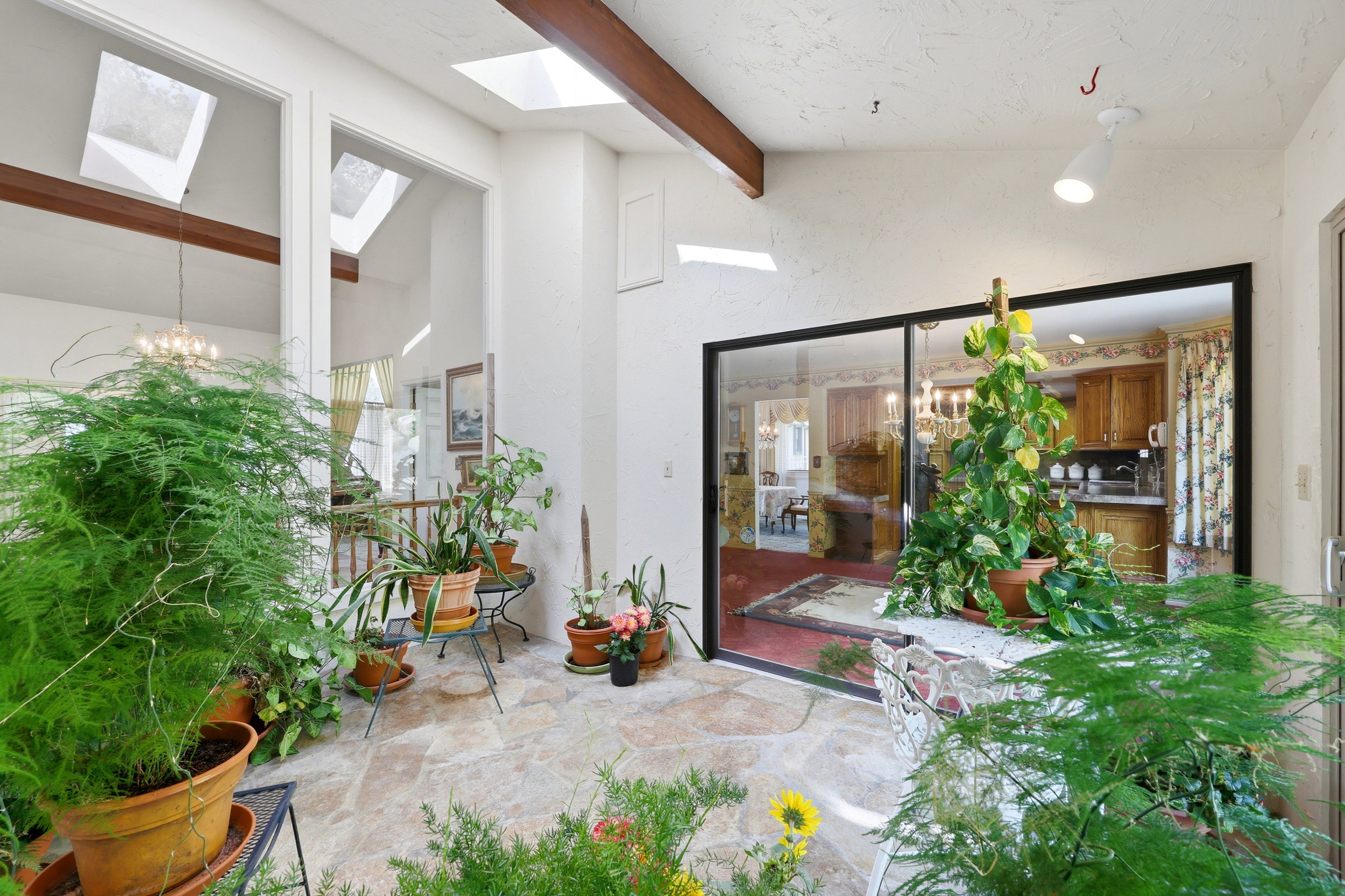 Sunroom featuring stone tile flooring, exposed wood beams, multiple skylights, vaulted ceilings, and sliding glass doors