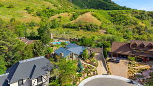 Stone exterior property with a metal roof, featuring structured landscaping, a private driveway, and an outdoor pool area with surrounding hardscaping