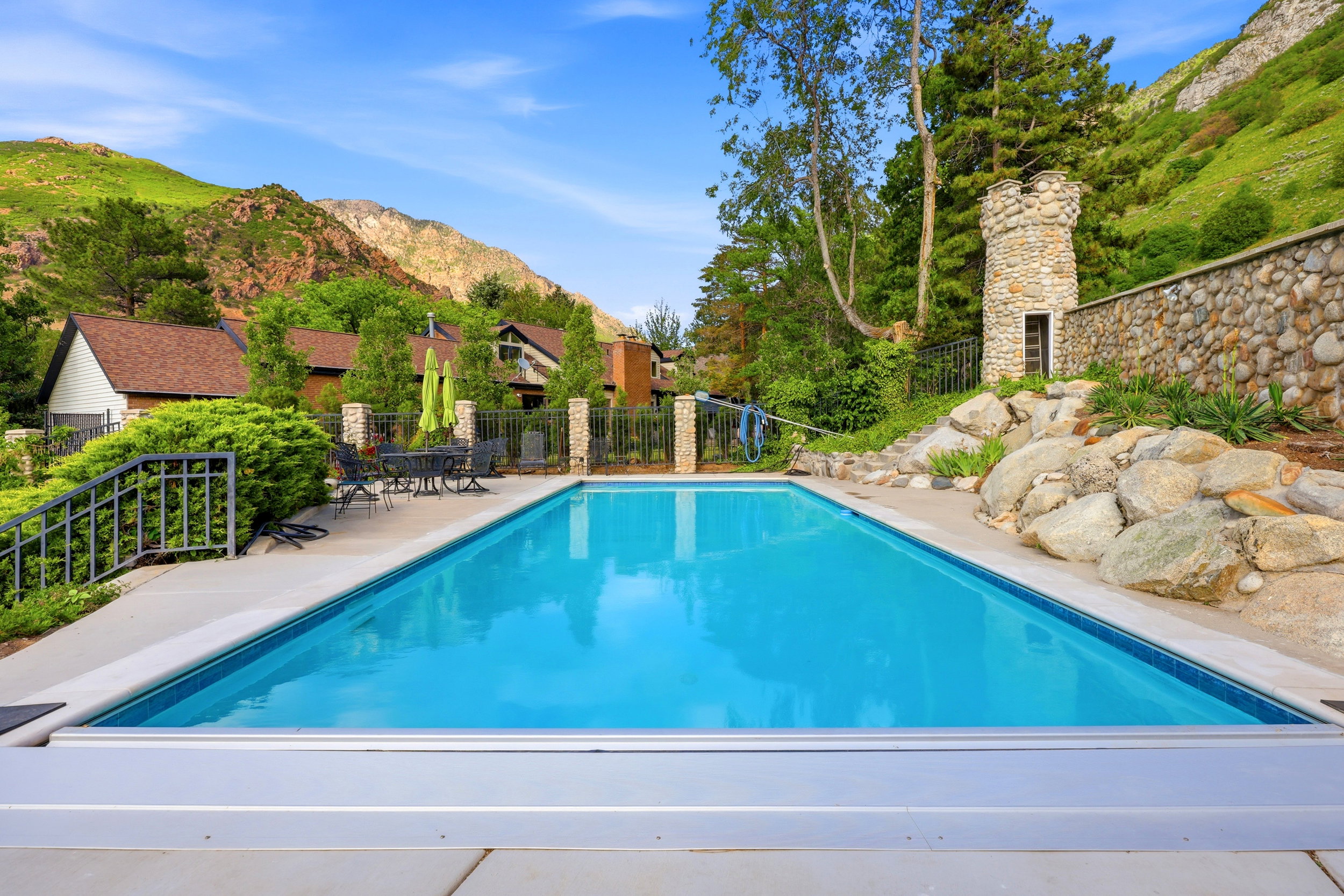 In-ground swimming pool with a surrounding concrete patio, stone retaining wall, and a stone tower structure