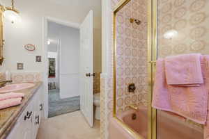 Bathroom featuring a pink tub and coordinated wall tiles, a glass shower enclosure with brass-finish framing, a vanity with a pink sink, a stone-finish countertop, and white cabinetry with dark hardware