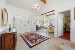 Vaulted entry foyer featuring a crystal chandelier, irregular flagstone flooring, and double entry doors with decorative glass inserts
