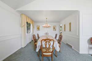 Dining area featuring a chandelier, wall molding, neutral-toned curtains, and blue patterned carpeting