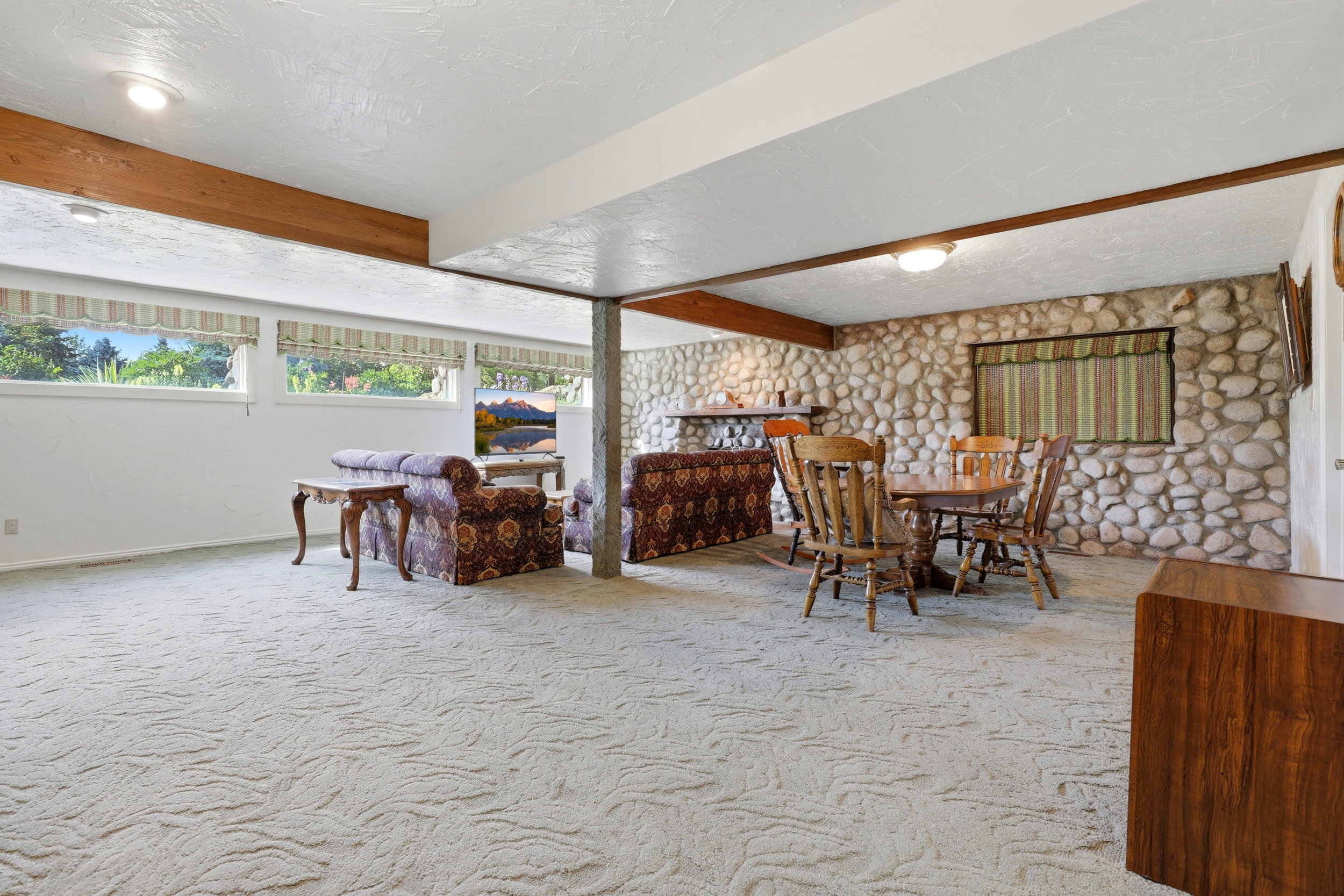 Spacious room featuring light-colored carpet flooring, a stone accent wall, and multiple windows