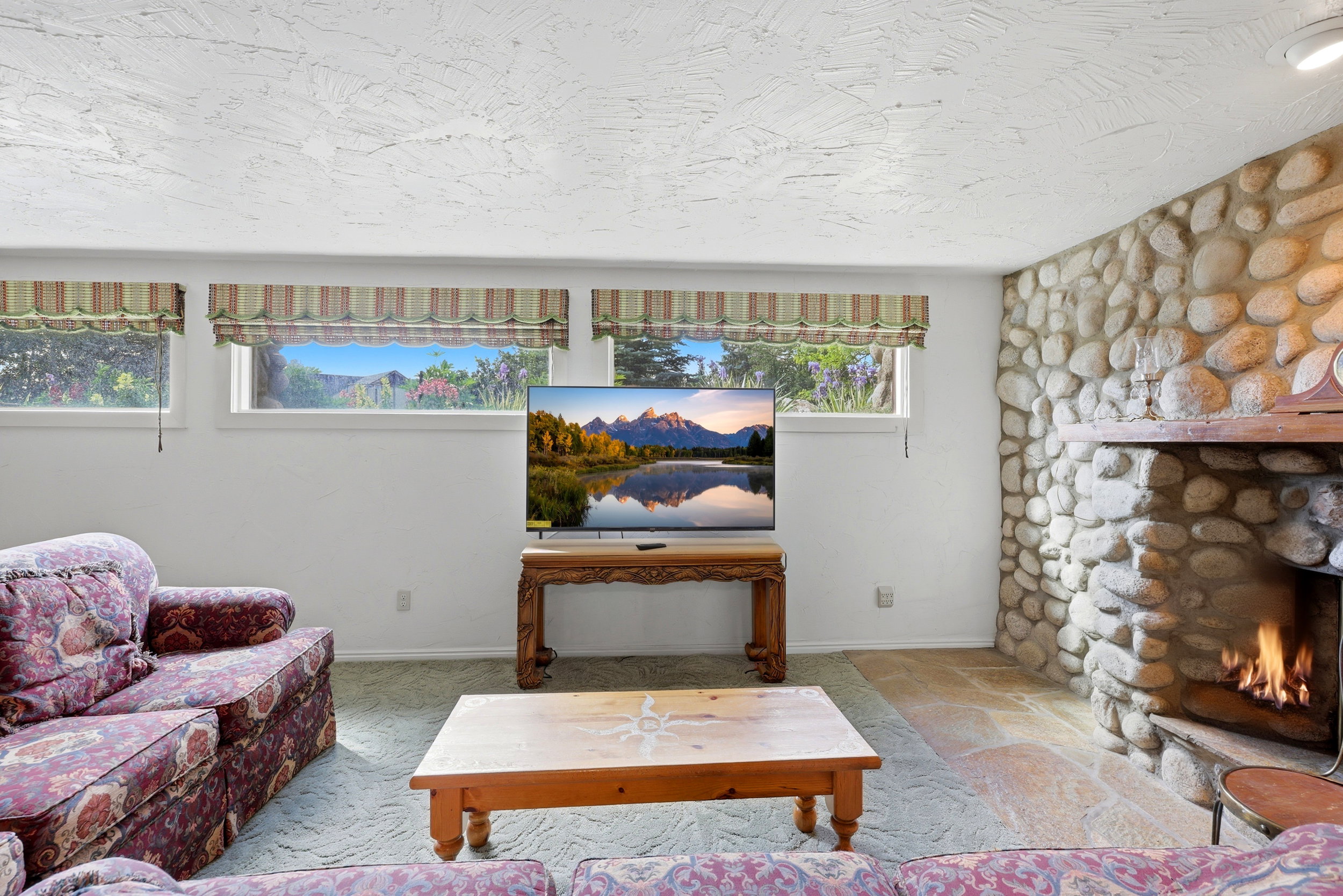 Living area featuring a floor-to-ceiling stone fireplace with a wood mantle, stone flooring, and multiple windows