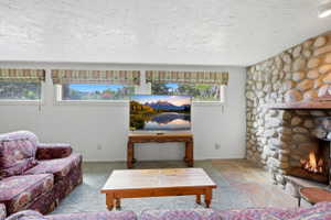 Living area featuring a floor-to-ceiling stone fireplace with a wood mantle, stone flooring, and multiple windows