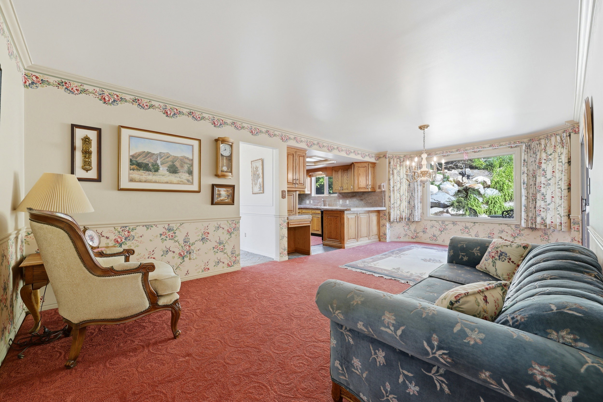 Open-concept living area featuring a large picture window, a chandelier, and red patterned carpeting