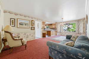 Open-concept living area featuring a large picture window, a chandelier, and red patterned carpeting