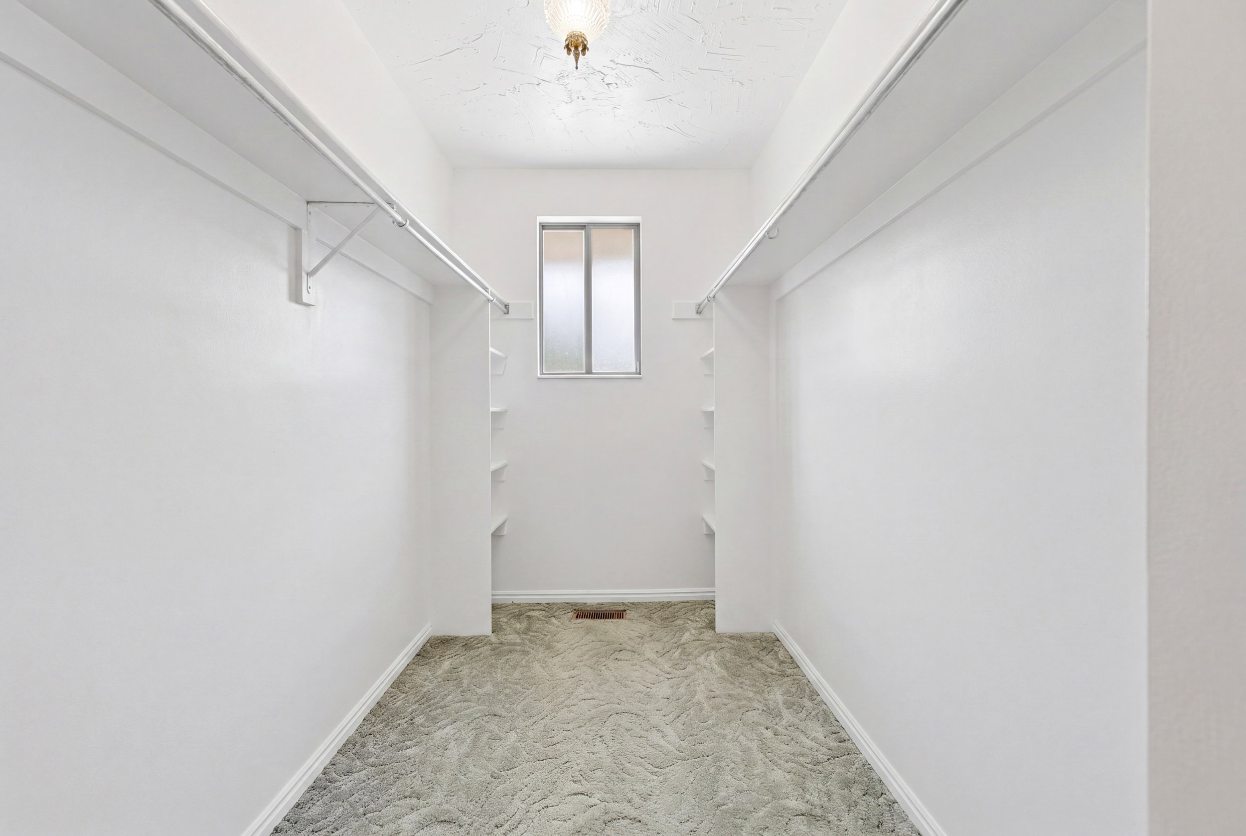 Spacious walk-in closet featuring white walls, light-toned patterned carpet, dual shelving, and hanging rods