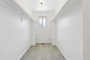 Spacious walk-in closet featuring white walls, light-toned patterned carpet, dual shelving, and hanging rods